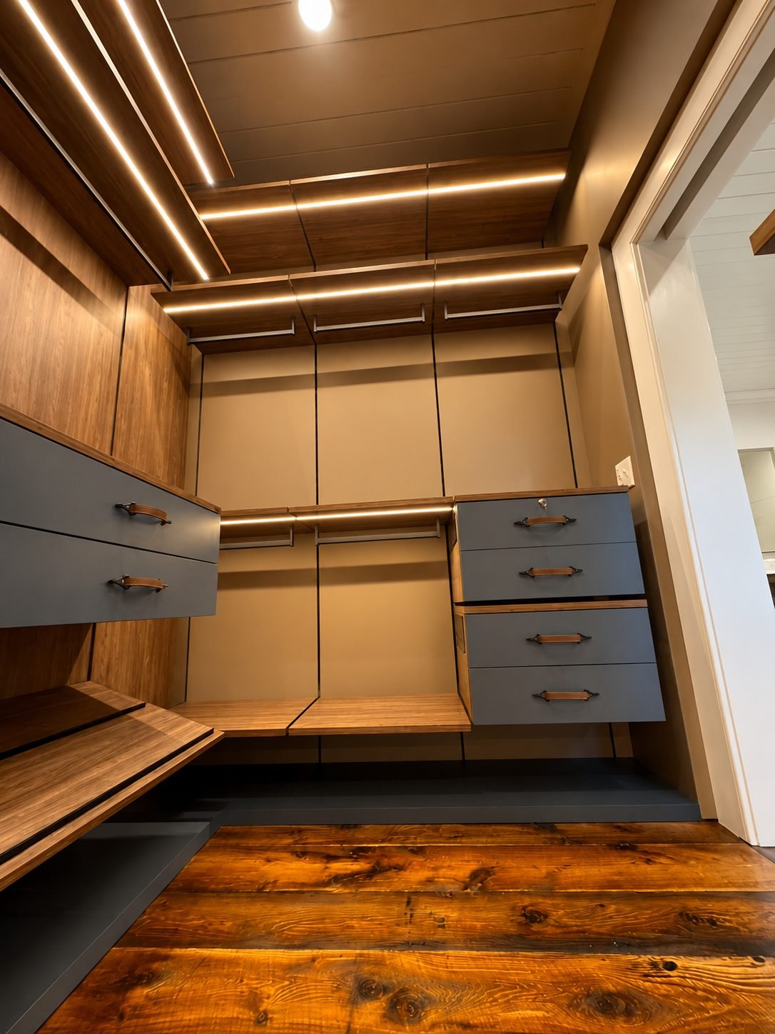 Walnut dressing room corner with slate-blue leather-pull drawers and reclaimed wood floor, opening to a hallway